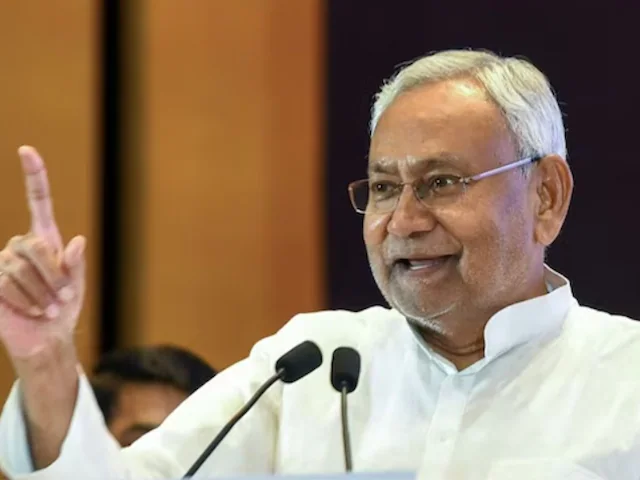 తెల్లని కుర్తా ధరించి, మైక్రోఫోన్ల ముందు చూపుడు వేలు ఎత్తి మాట్లాడుతున్న నితీష్ కుమార్
